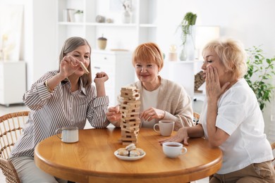 Friendship. Senior women building tower with wooden blocks at wooden table indoors