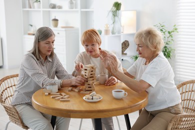 Photo of Friendship. Senior women building tower with wooden blocks at wooden table indoors