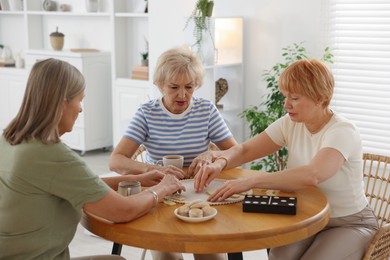 Photo of Friendship. Senior women playing dominoes at wooden table indoors