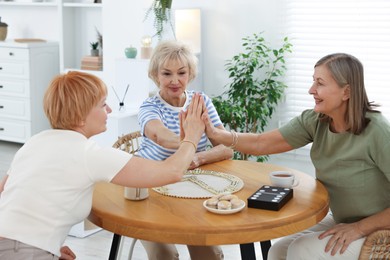 Photo of Friendship. Senior women playing dominoes at wooden table indoors