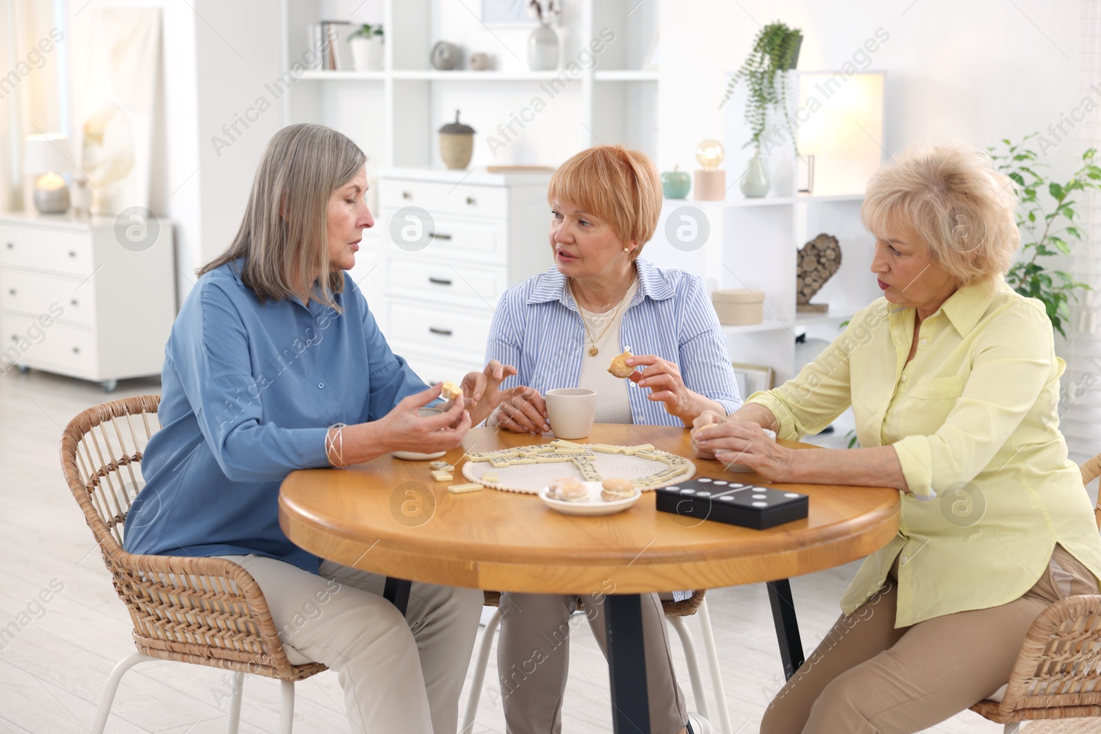 Photo of Friendship. Senior women enjoying hot drinks and cookies at table indoors