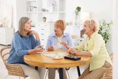 Friendship. Senior women enjoying hot drinks and cookies at table indoors