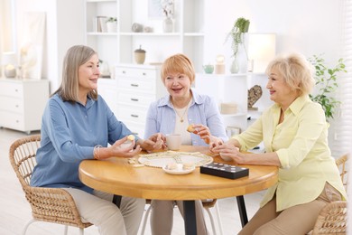 Friendship. Senior women enjoying hot drinks and cookies at table indoors