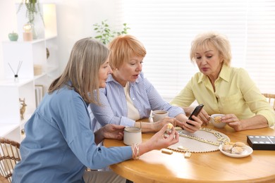 Photo of Friendship. Senior women watching something on smartphone at table indoors