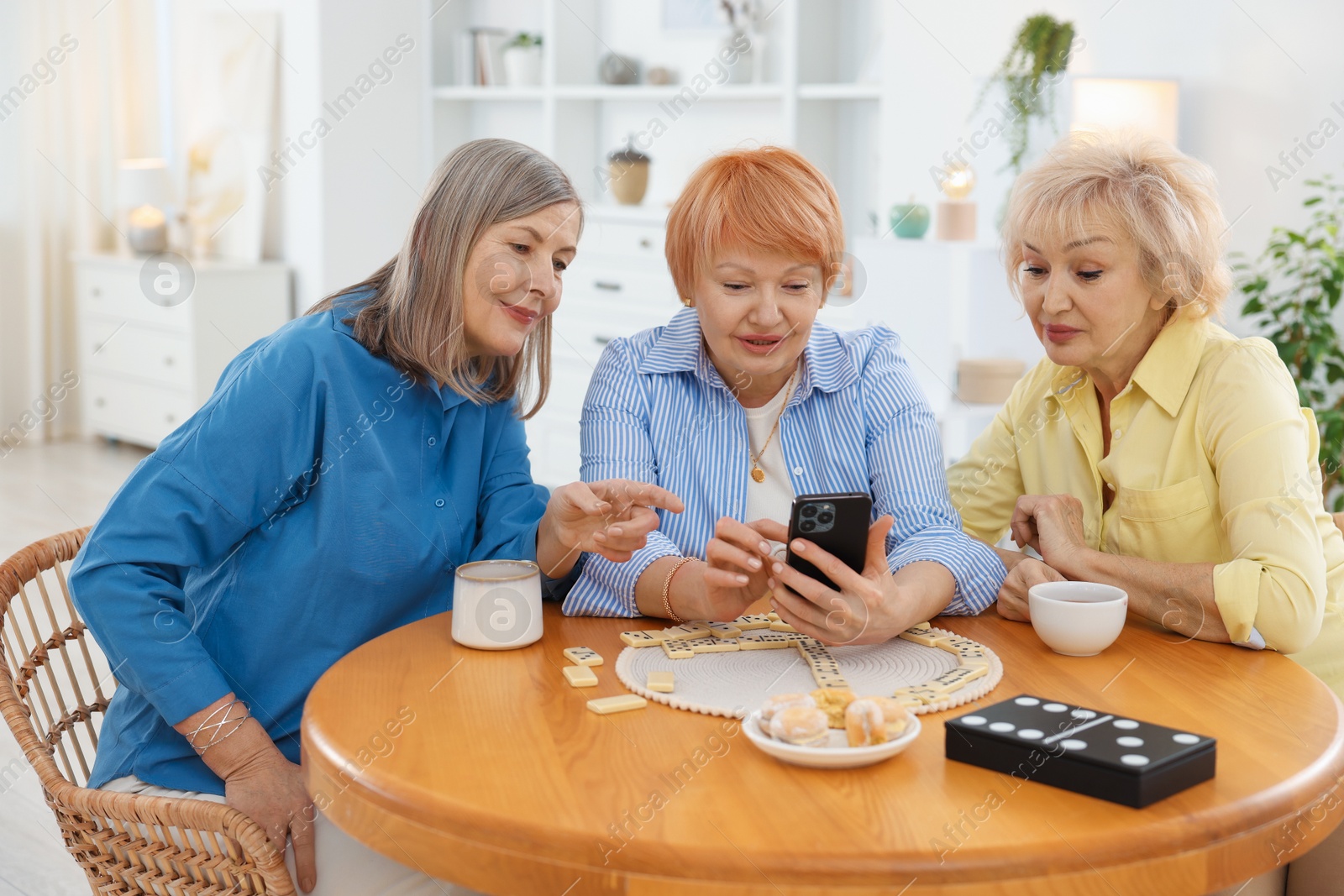 Photo of Friendship. Senior women watching something on smartphone at table indoors