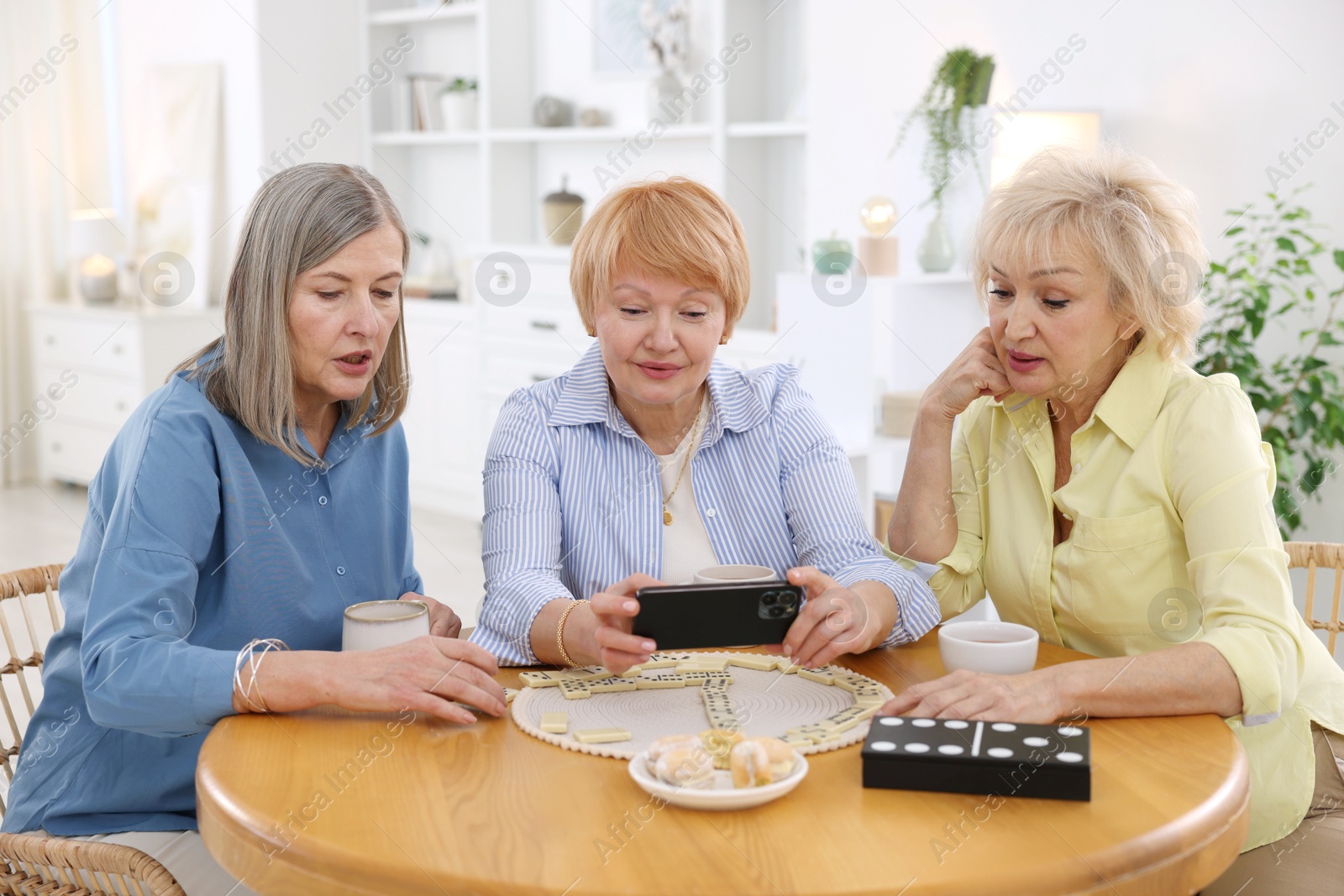 Photo of Friendship. Senior women watching something on smartphone at table indoors