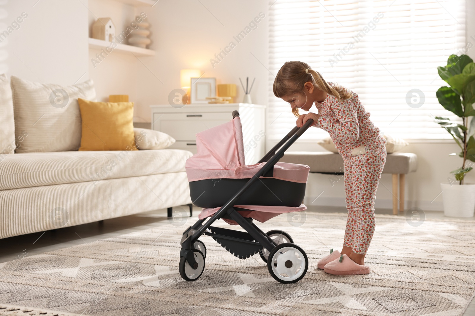 Photo of Cute little girl with doll stroller at home