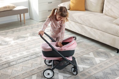 Photo of Cute little girl with doll stroller at home