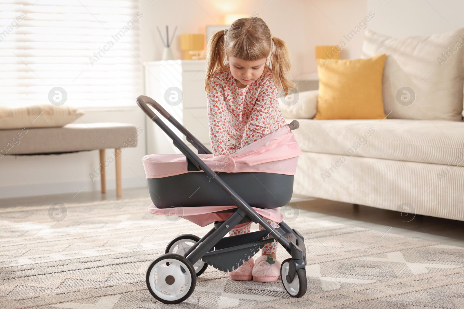 Photo of Cute little girl with doll stroller at home