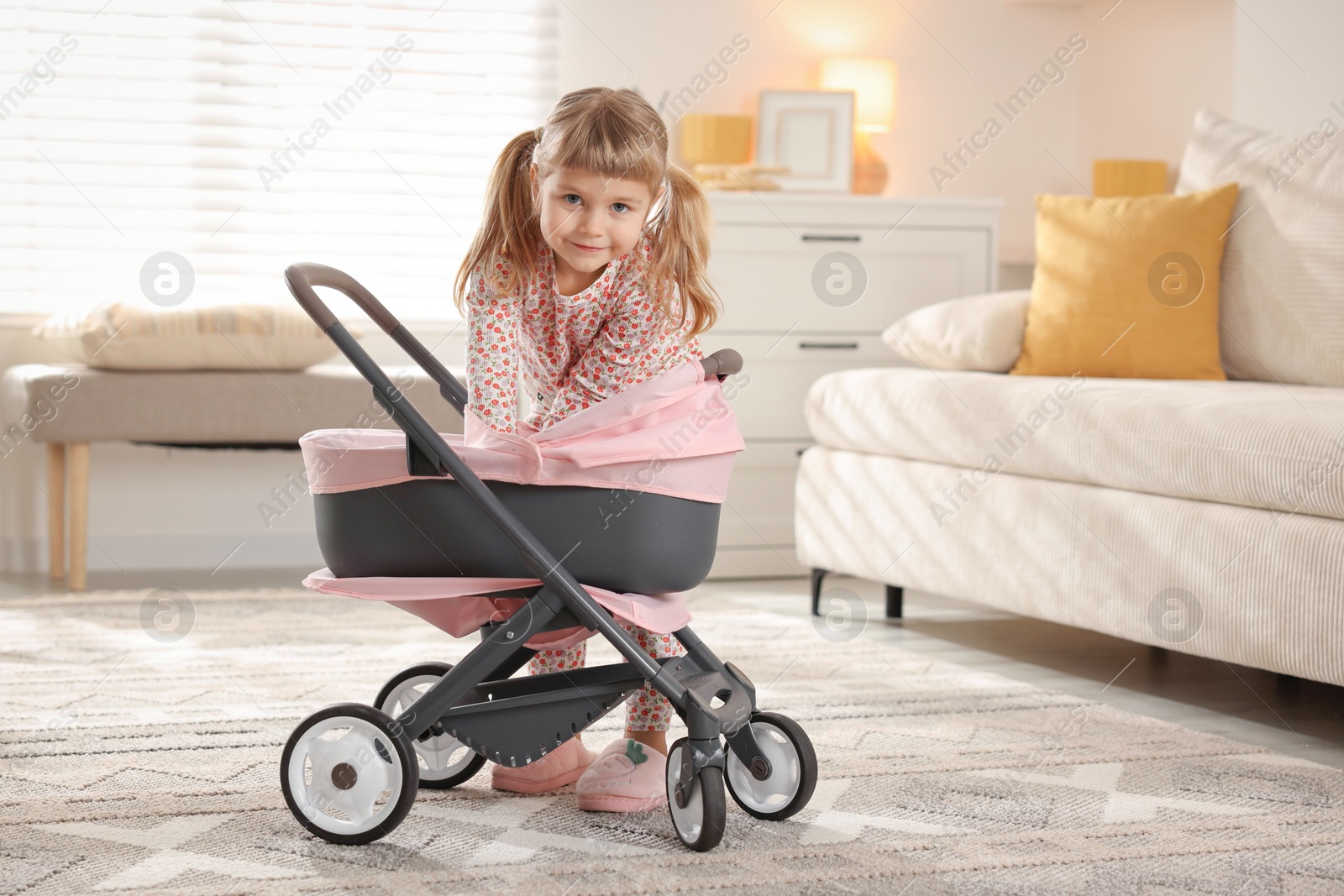 Photo of Cute little girl with doll stroller at home