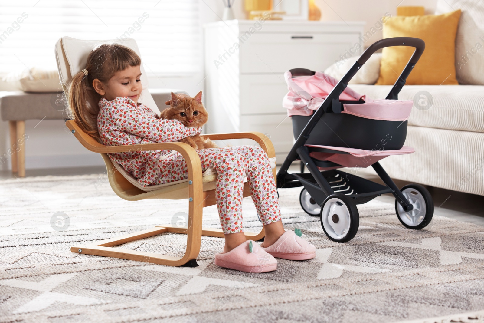 Photo of Cute little girl with her ginger cat sitting in armchair at home