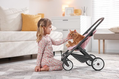 Photo of Cute little girl with her ginger cat in doll stroller at home