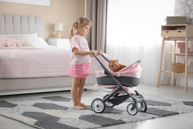 Cute little girl with her ginger cat in doll stroller at home