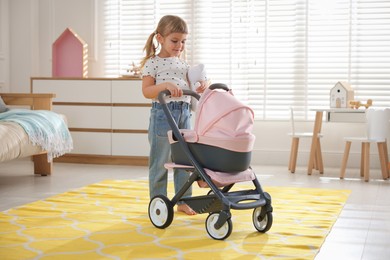 Photo of Cute little girl with doll stroller and teddy bear at home