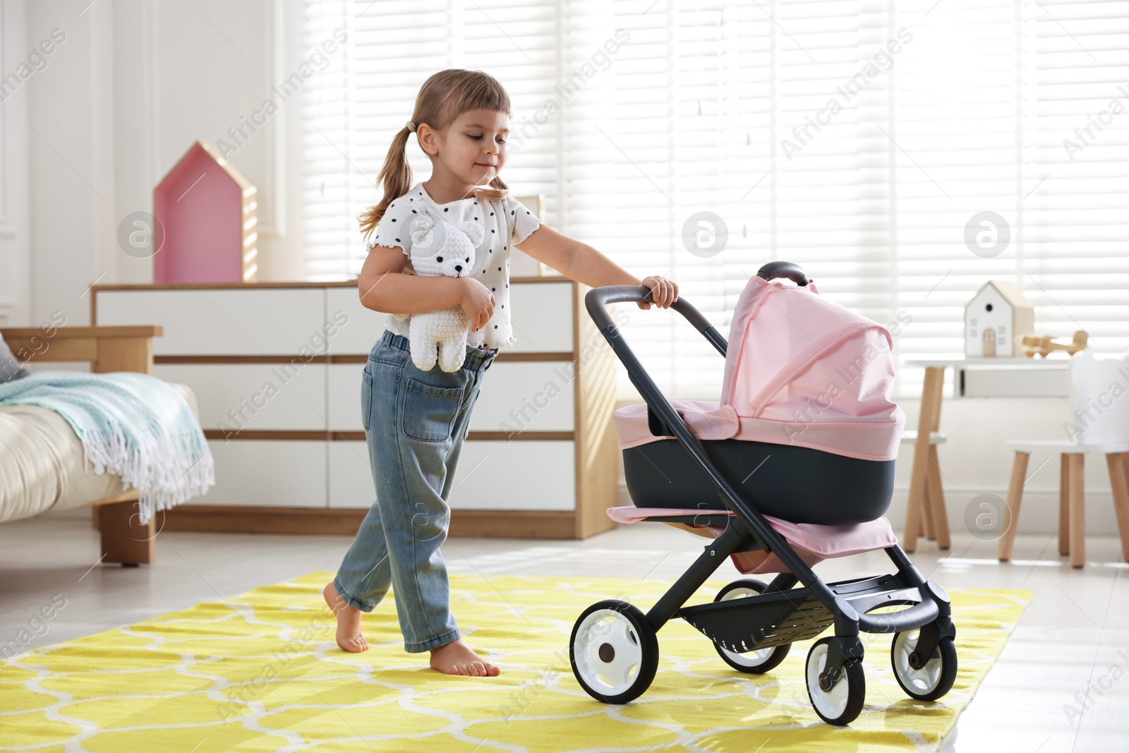 Photo of Cute little girl with doll stroller and teddy bear at home