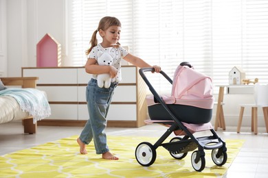 Photo of Cute little girl with doll stroller and teddy bear at home