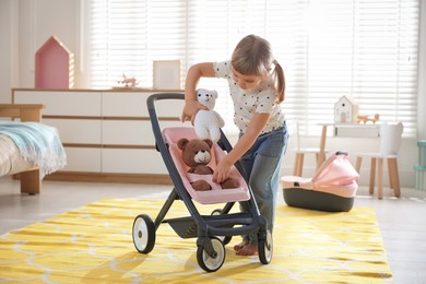 Cute little girl playing with doll stroller and teddy bears at home