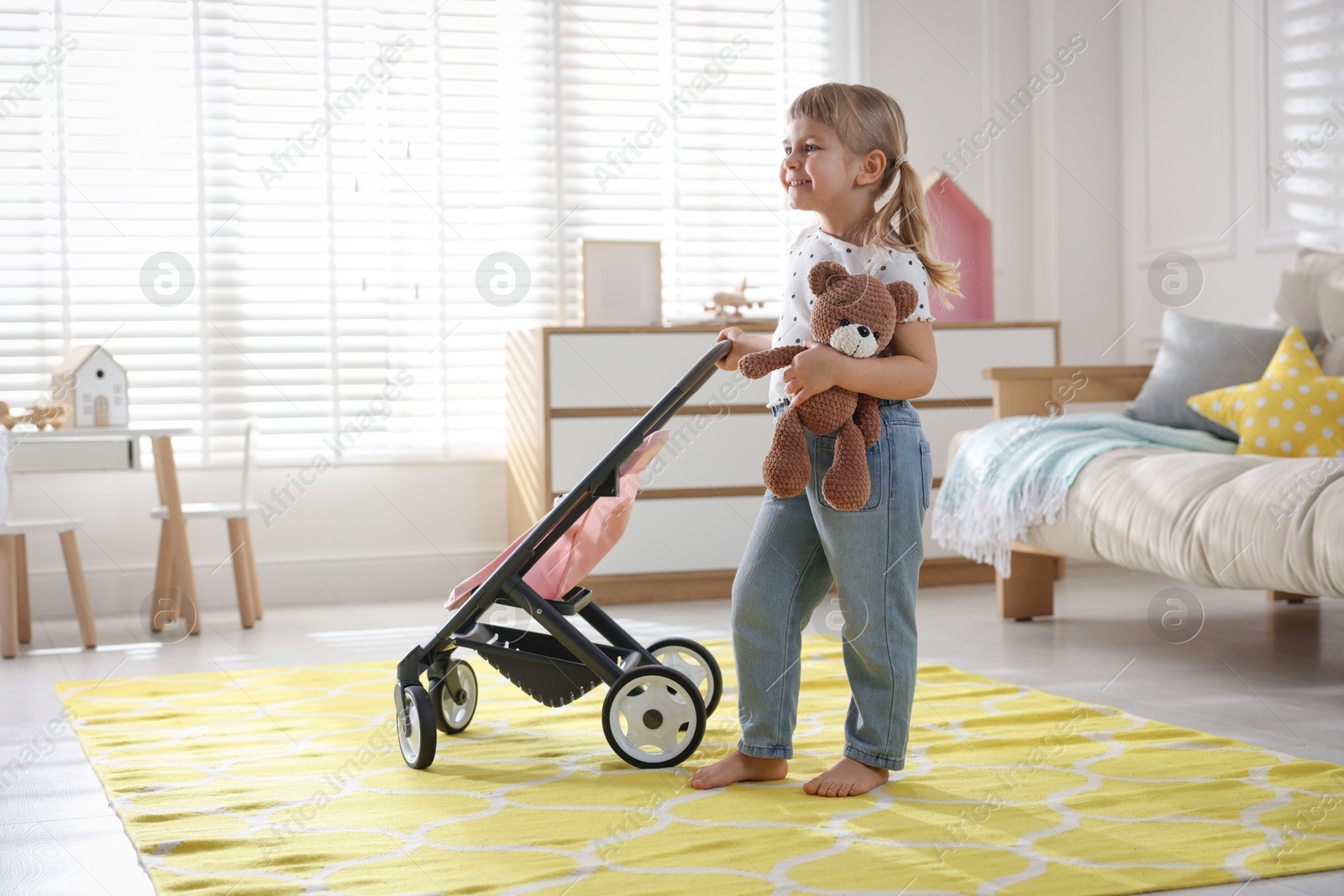 Photo of Cute little girl with doll stroller and teddy bear at home