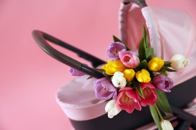 Photo of Stylish doll stroller and tulips on pink background, closeup. Kid's toy