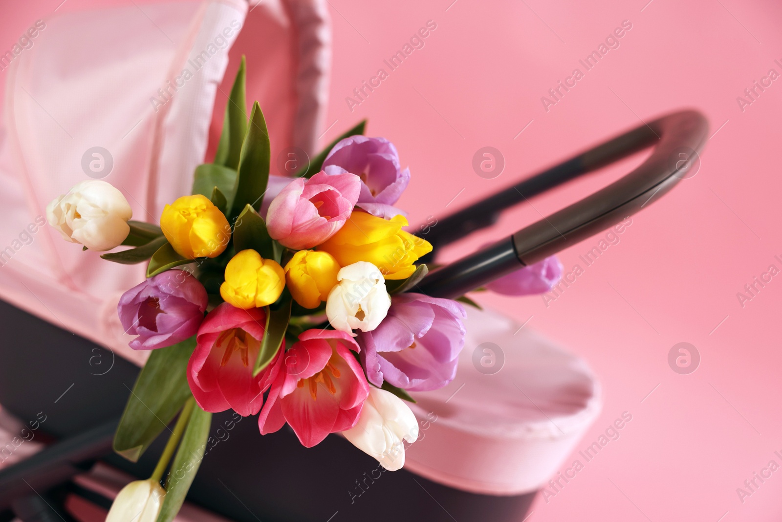 Photo of Stylish doll stroller and tulips on pink background, closeup. Kid's toy