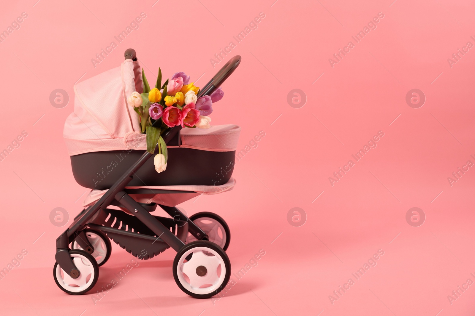 Photo of Stylish doll stroller and tulips on pink background, space for text. Kid's toy