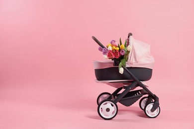 Photo of Stylish doll stroller and tulips on pink background, space for text. Kid's toy