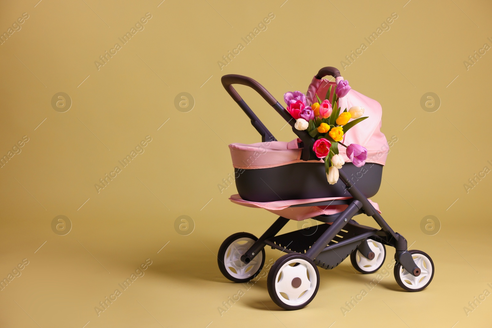 Photo of Stylish doll stroller and tulips on olive background, space for text. Kid's toy