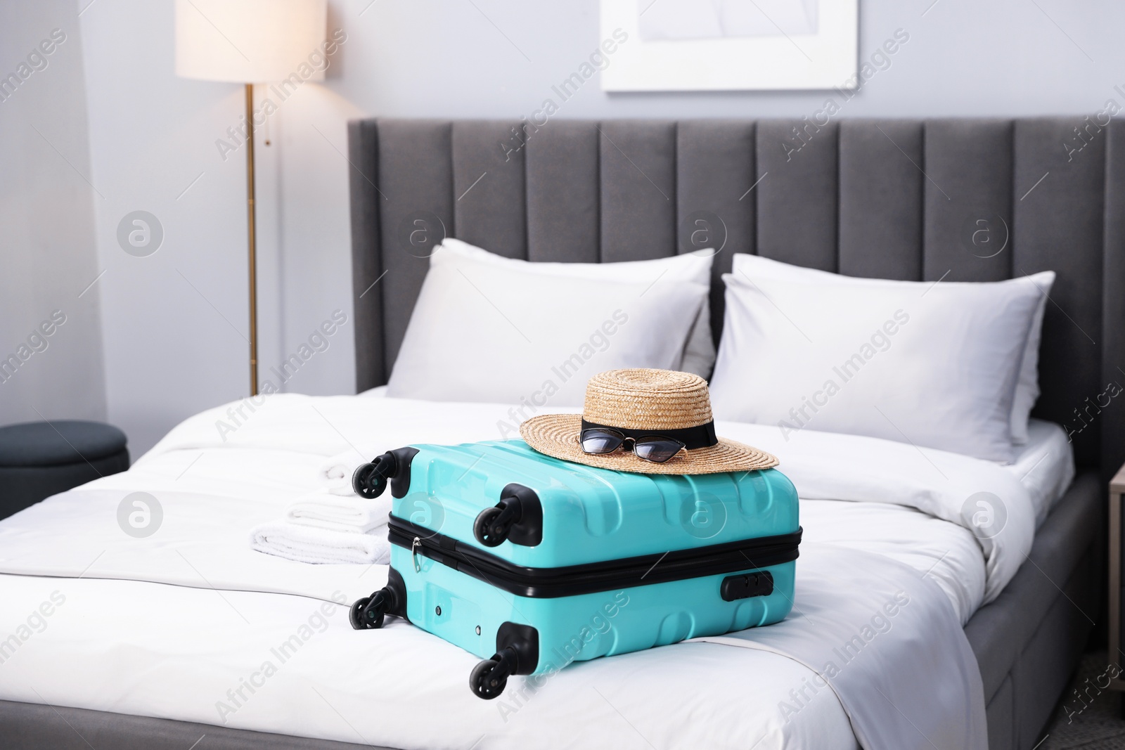 Photo of Suitcase with hat and sunglasses on bed in hotel room