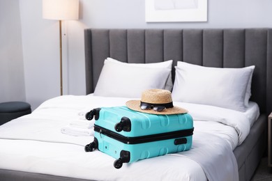 Suitcase with hat and sunglasses on bed in hotel room