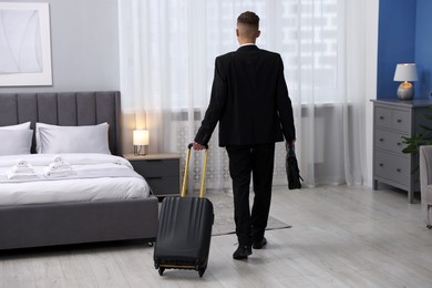 Photo of Businessman with suitcase in hotel room, back view