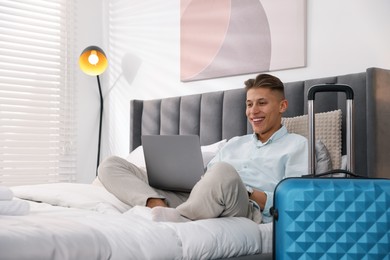 Man with laptop on bed in his hotel room. Space for text