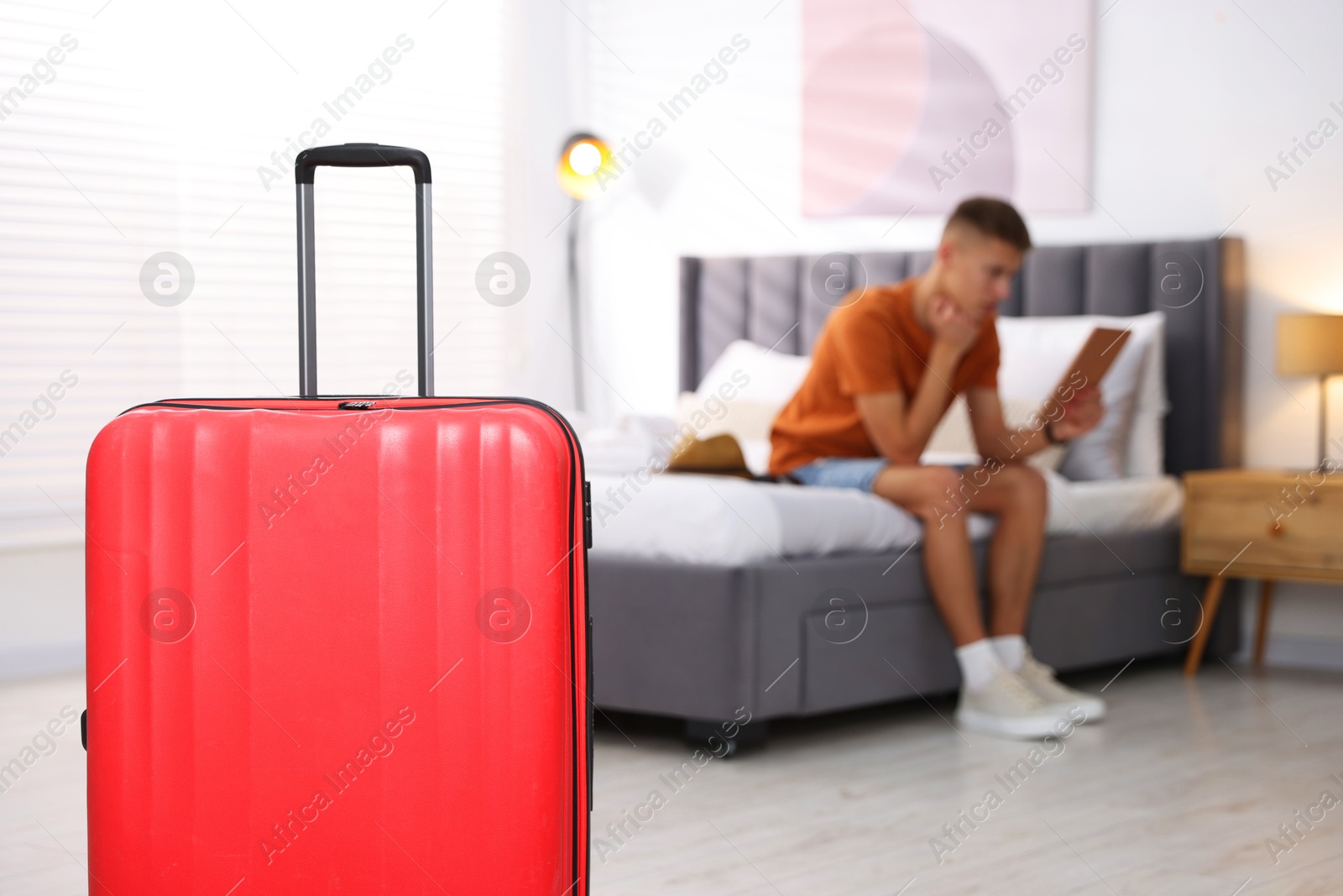 Photo of Suitcase and man with tablet on bed in his hotel room, selective focus