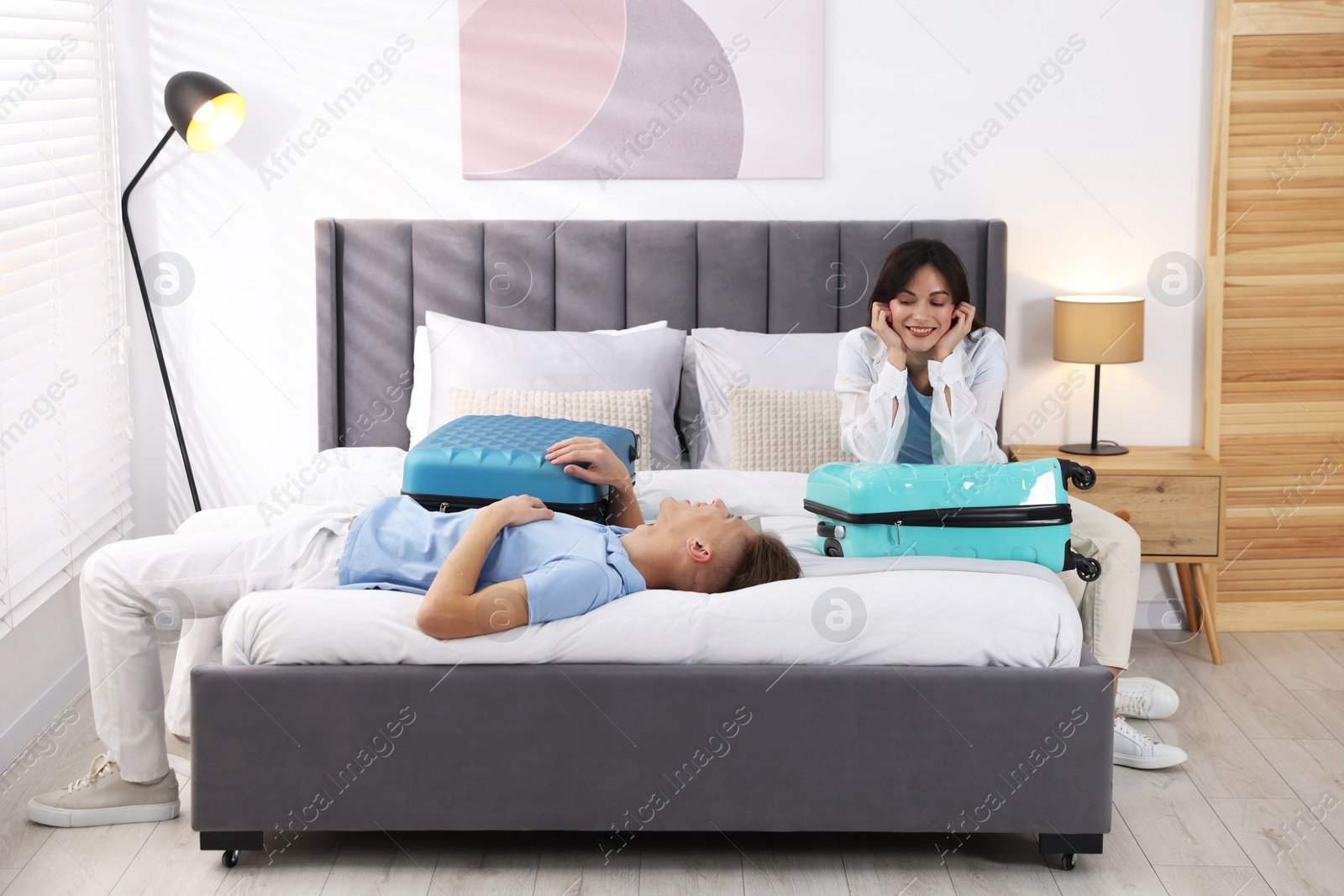 Photo of Happy couple with suitcases on bed in hotel room