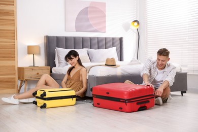 Happy couple unpacking their suitcases in hotel room