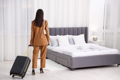 Businesswoman with suitcase in her hotel room, back view