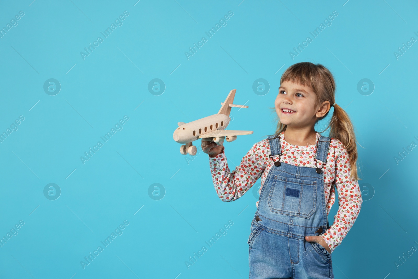 Photo of Happy little girl playing with toy plane on light blue background. Space for text