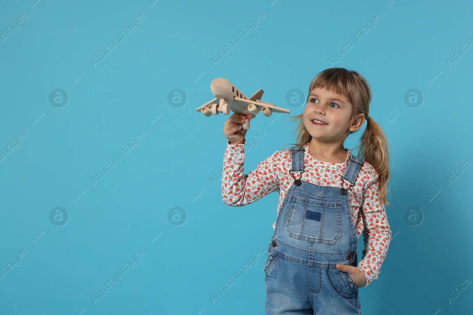 Photo of Happy little girl playing with toy plane on light blue background. Space for text