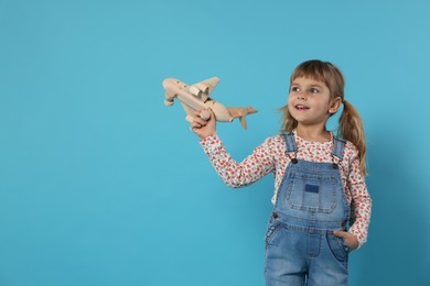 Happy little girl playing with toy plane on light blue background. Space for text