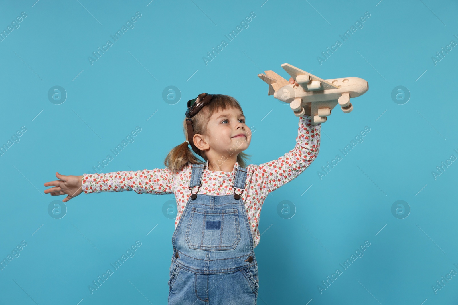 Photo of Cute little girl playing with toy plane on light blue background