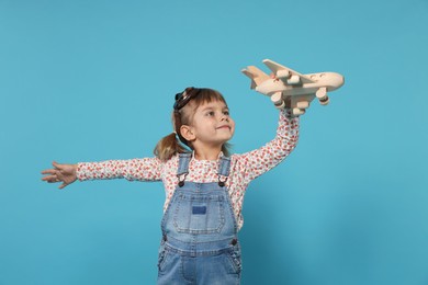 Cute little girl playing with toy plane on light blue background