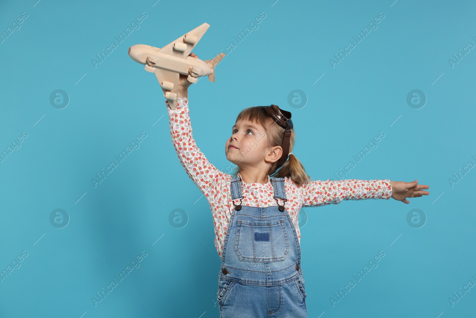 Photo of Cute little girl playing with toy plane on light blue background