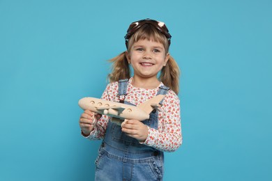 Happy little girl playing with toy plane on light blue background