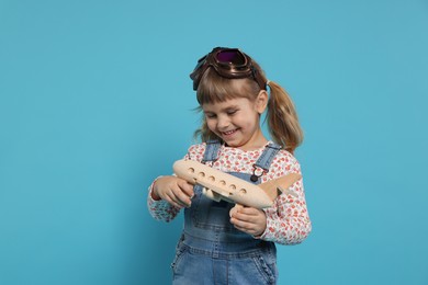 Happy little girl playing with toy plane on light blue background