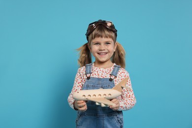 Happy little girl with toy plane on light blue background