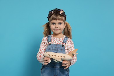 Cute little girl with toy plane on light blue background