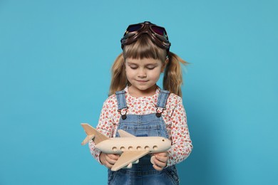 Cute little girl with toy plane on light blue background