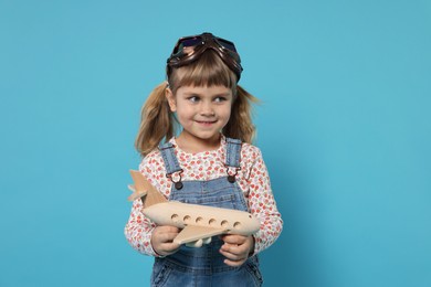 Cute little girl with toy plane on light blue background