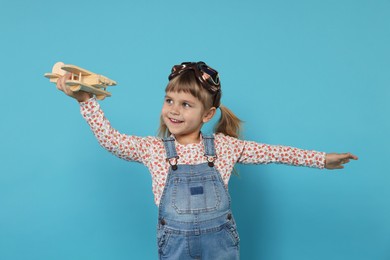 Photo of Happy little girl playing with toy plane on light blue background