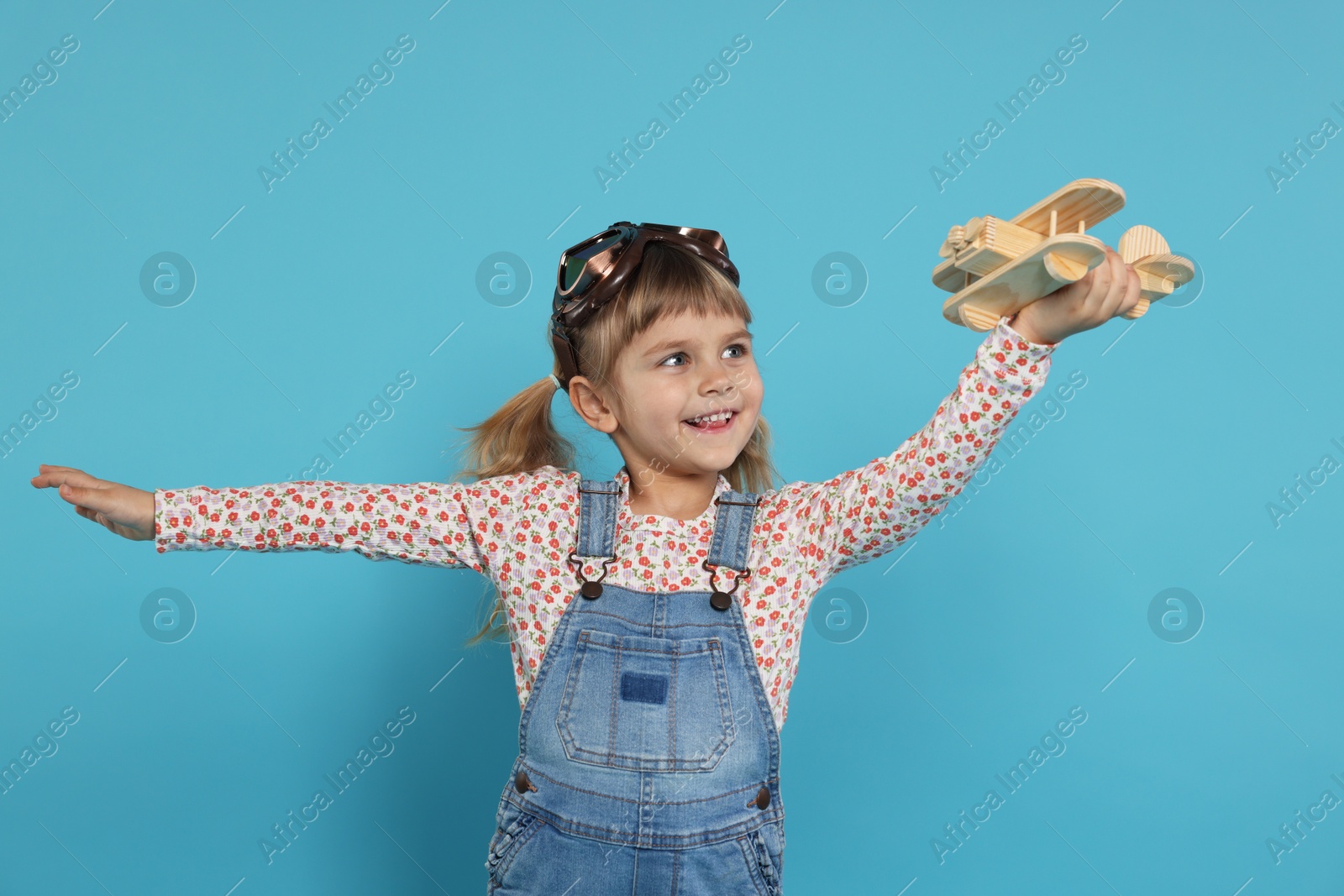 Photo of Happy little girl playing with toy plane on light blue background