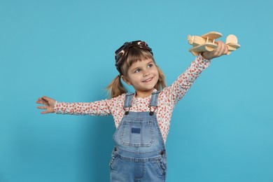 Photo of Happy little girl playing with toy plane on light blue background